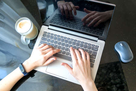 top view of woman's hands typing on laptop with notebook and items on black background.の写真素材