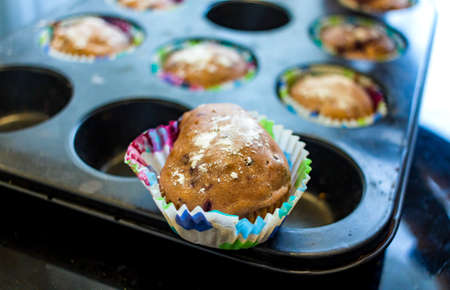 Freshly baked cupcake cakes in two varieties in a muffin tin, one standing outside, selected focus, narrow depth of field.の写真素材
