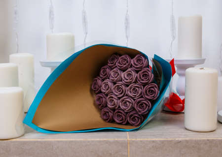 bouquet of chocolate flowers, beautifully packaged, lies on the fireplace among candles, an unusual edible giftの写真素材