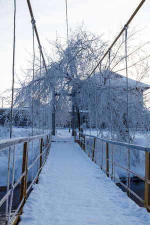 suspended pedestrian bridge on the background of winter frost and suburban houses. Frozen branches with frostの写真素材