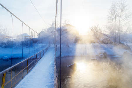 winter landscape with a snow-covered river bank, trees covered with hoarfrost, fog and rising sun over riverの写真素材