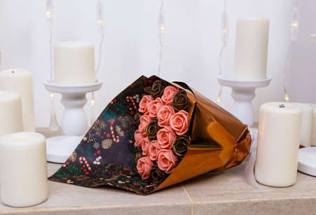 bouquet of chocolate flowers, beautifully packaged, lies on the fireplace among the candles, an unusual edible giftの写真素材