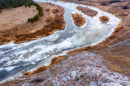 aerial top view of river bend with snowy frozen shore and bare trees in winter dayの写真素材