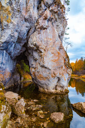 A rock with gap on the river among autumn nature and yellow foliage, an autumn landscape with stones, water and the reflection of autumn trees.の写真素材