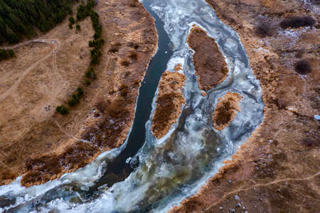 Top down view over snowy river valley with partially frozen river.の写真素材