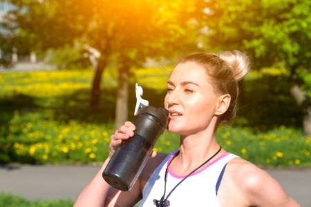 Young blonde sportswoman doing exercise drinking bottle of water at the parkの写真素材