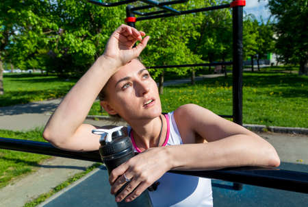 tired girl on the workout site with a bottle in her hand, tired after training, bright sunny dayの写真素材
