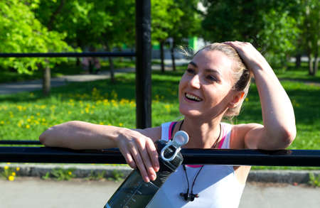 tired smiling girl on the workout site with a bottle in her hand, tired after training, bright sunny dayの写真素材