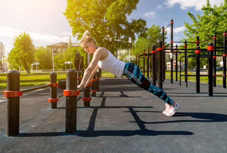 picture of a fit young woman stretching in a city park. A bar for warming up on the uneven bars, bright sunny day.の写真素材