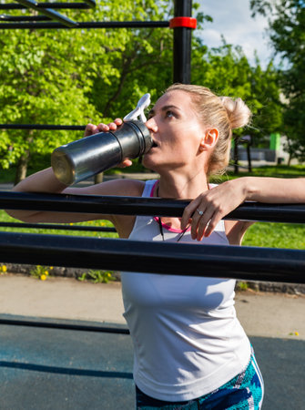 Young blonde sportswoman doing exercise drinking bottle of water at parkの写真素材