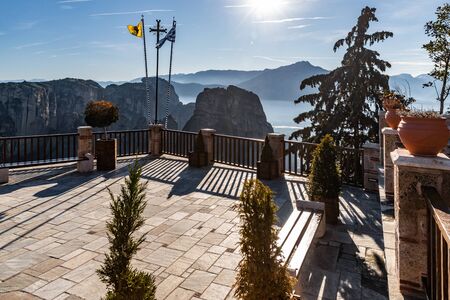 Kalambaka, Greece, Terrace of monastery Varlaam and breathtaking pictures of valley and landmark canyon of Meteora at sunset, magic shadows, flags, Benchesの写真素材