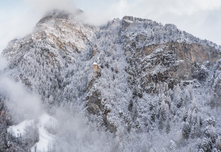 Aerial view of mountain with boundary tower, forest underneath fog, slopes with snow covered in...