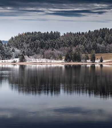 Landscape of a specular reflection in the lake, a dry grass, a cane and snags in the foreground, mountains and the forest on a background, ice on water, grass is covered with hoarfrost, tranquillityの写真素材