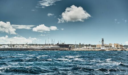 Spain, Formentera, 29 April 2018: The harbor of famous Formentera, a lighthouse, azure water, boats, sunny weather, without peopleの写真素材