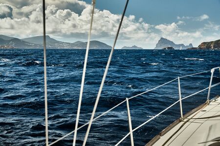 The view of the sea and mountains from the sailboat, edge of a board of the boat, slings and ropes, splashes from under the boat, sunny weather, dramatic skyの写真素材
