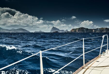The view of the sea and mountains from the sailboat, edge of a board of the boat, slings and ropes, splashes from under the boat, sunny weather, dramatic skyの写真素材