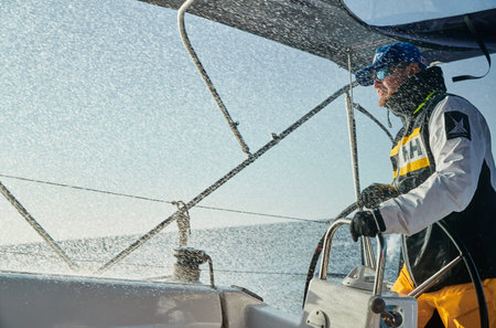 Spain, Malorca, 29 April 2018: The brutal man at yacht steering wheel during a storm, splashes fly to a face, Extreme entertainment, the person is dressed in waterproof clothes and sunglasses,のeditorial素材