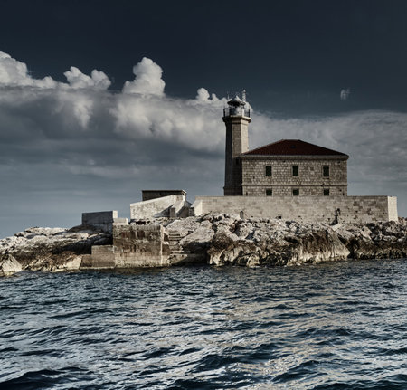 The island with a lighthouse at sunset, big white clouds are on background, reflection is on water, close upの写真素材