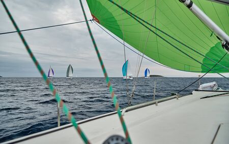Croatia, Adriatic Sea, 19 September 2019: The race of sailboats, the team sits on the edge of a boat board, bright colors, view of participants of race from other boat through ropesの写真素材