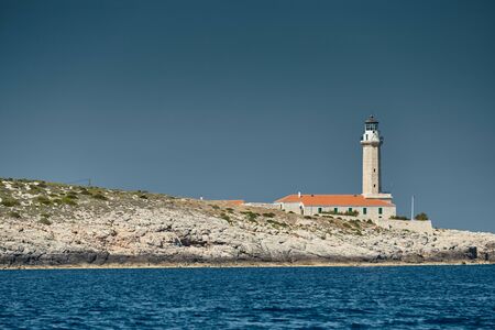 The lighthouse on the island in Croatia nearby Vis at sunset, a rocky coast, ladder to a beaconの写真素材