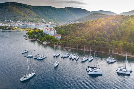 Aerial view of marina Vis at sunset, Croatia, a lot of chaotically standing boats in a bay, roofs of orange color, sunshine, hills with green trees, ferry stationの写真素材