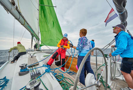 Croatia, Adriatic Sea, 19 September 2019: The race of sailboats, the team sits on the edge of a boat board, team work, intense fight, bright colors, other participants of race on a backgroundのeditorial素材