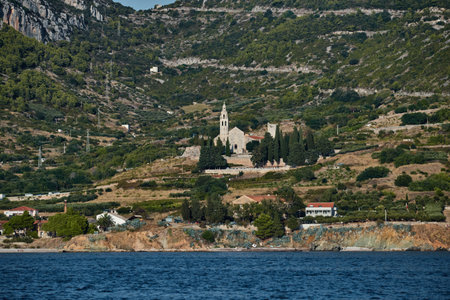 Seaview of the cathedral St.Nicholas in Komiza city at sunset - the one of numerous port towns in Croatia, green hills, mountain is on backgroundの写真素材