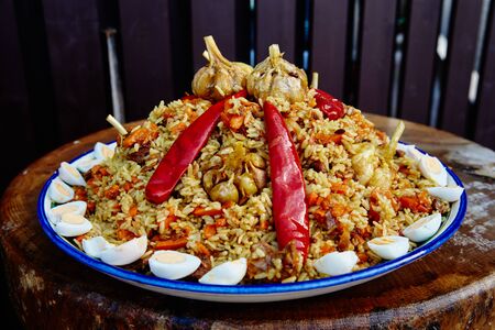 National Uzbek dish pilaf. Cooking in a cauldron on fire. Spread beautifully on a national plate lyagan rice, from above slices of the cut meat and decorate with red pepper and garlicの写真素材