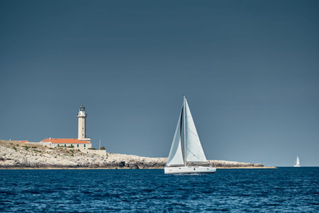 Croatia, 15 September 2019: Seascape of the sailboat in the foreground, the lighthouse on the island is on background, Croatia, at sunset, a rocky coast, ladder to a beacon, a small capeのeditorial素材