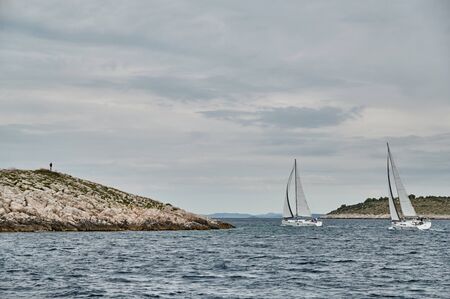 Seascape of the sailboat in the foreground, the men on the island is on background, Croatiaの写真素材