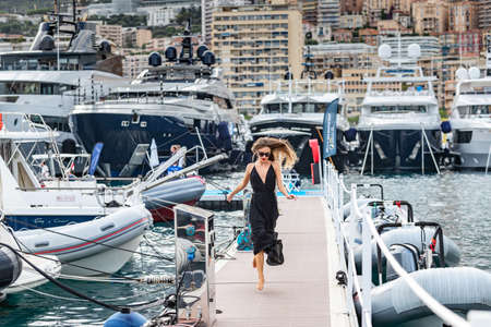 Monaco, Monte-Carlo, 27 September 2019: The elegant girl dressed in an evening dress of black color and sunglasses runs on pier in Monaco Yacht Show, gorgeous woman, sexual red lipsのeditorial素材