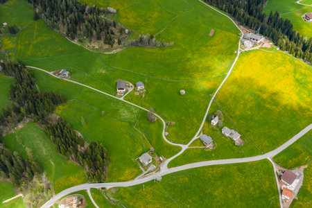 Aerial view of improbable green meadows of Italian Alps, green slopes of the mountains, huge clouds over a valley, roof tops of houses, Dolomites on background, sunshines through cloudsの写真素材