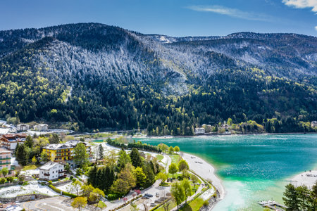 The Improbable aerial landscape of village Molveno, Italy, azure water of lake, empty beach, snow covered mountains Dolomites on background, roof top of chalet, sunny weather, a piers, coastline,の写真素材
