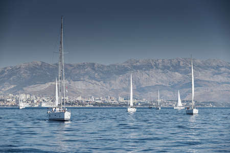 Croatia, Adriatic Sea, 15 September 2019: The race of sailboats, a regatta, reflection of sails on water, Intense competition, bright colors, island with windmills are on backgroundのeditorial素材