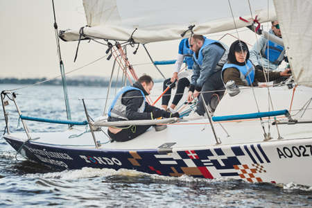 Russia, St.Petersburg, 05 September 2020: Participants of a sailing regatta on the sailboat, pull ropes, water splashes in the foreground, focus on splashesのeditorial素材