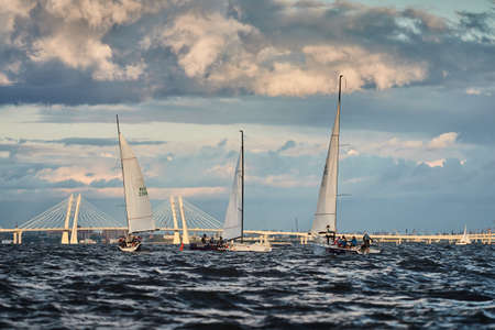 Russia, St.Petersburg, 23 July 2021: Competition of Three sailboats on the horizon in sea at sunset, the amazing storm sky of different colors, race, big waves, sail regatta, cloudy weatherのeditorial素材