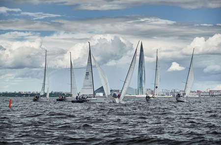 Russia, St. Petersburg, 23 July 2021: Competition of few sailboats in regatta at storm weather, skyscraper Lakhta center by Gazprom oil company on background, race, big waves, team workのeditorial素材