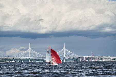 Russia, St. Petersburg, 23 July 2021: Competition of sailboats on the horizon in sea at sunset, the amazing storm sky of different colors, race, big waves, sail regatta, sun beams, team workのeditorial素材