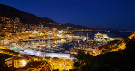 Aerial view of port Hercules in Monaco - Monte-Carlo at dusk, a lot of yachts and boats are moored in marina, cityscape with night illumination, magic reflection on water, mountain, mediterranean seaの写真素材