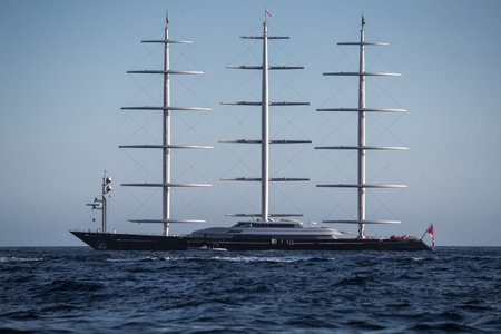 A huge sail yacht of conceptual design with three masts stands in the bay near Monaco at sunny day, the sails are lowered, the yacht spins around its anchor, left side of the sailboat, clear weatherの写真素材
