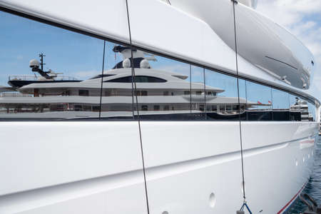Reflection of a boat on a glossy surface of a huge yacht at sunny day, the chrome plated handrail, megayacht is moored in portの写真素材