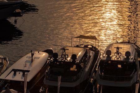 Top decks of luxury motor boats with sun reflections in port of Monaco at sunrise, glossy board, the chrome plated handrail, are moored in marina, water surface on backgroundの写真素材