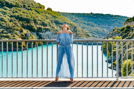 The beautiful girl in a blue dress and sunglasses poses on the bridge, the long chestnut hair, happy...