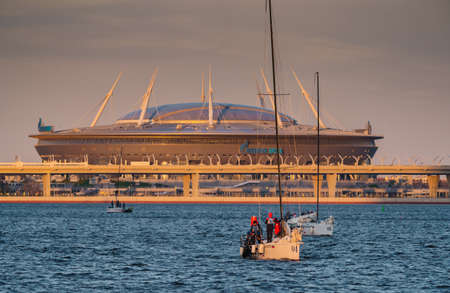 Russia, St. Petersburg, 20 May 2022: Sailing boats in the background of the new stadium Gazprom arena by the oil company Gazprom in sunset lightのeditorial素材