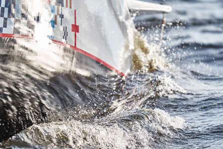water shatters against the glossy side of a sailing boat in a roll at sunset, splashes of water and glare of the sun, wavesの写真素材