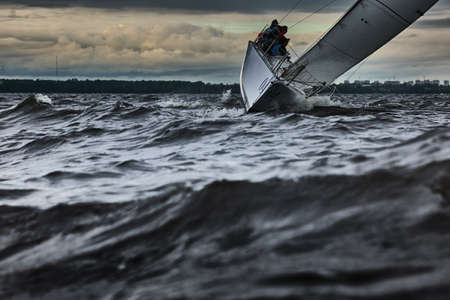 Sailboat in sea at stormy weather, stormy clouds sky orange sky, sail regatta, reflection of sail in the water, bigl waves of water,の写真素材