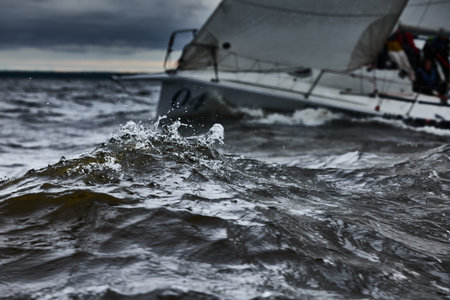 Splashes of water in sailing regatta, teamwork in sailing yacht at stormy weather, hot pursuit, clouds skyの写真素材