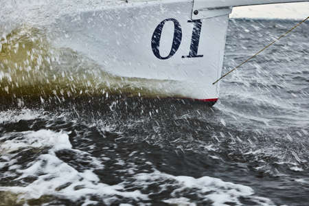 the bow of the boat cuts through the water, bowsprit of sailing yacht in sailing regatta at stormy weather, splashes of water, hot racing, number oneの写真素材