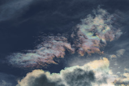 Diffraction of light on drops of supercooled water in clouds, rainbow clouds against the blue sky in clear sunny weather, irisation of cumulus clouds, optical phenomenon, spectral colorsの写真素材