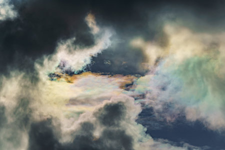Diffraction of light on drops of supercooled water in clouds, rainbow clouds against the blue sky in...